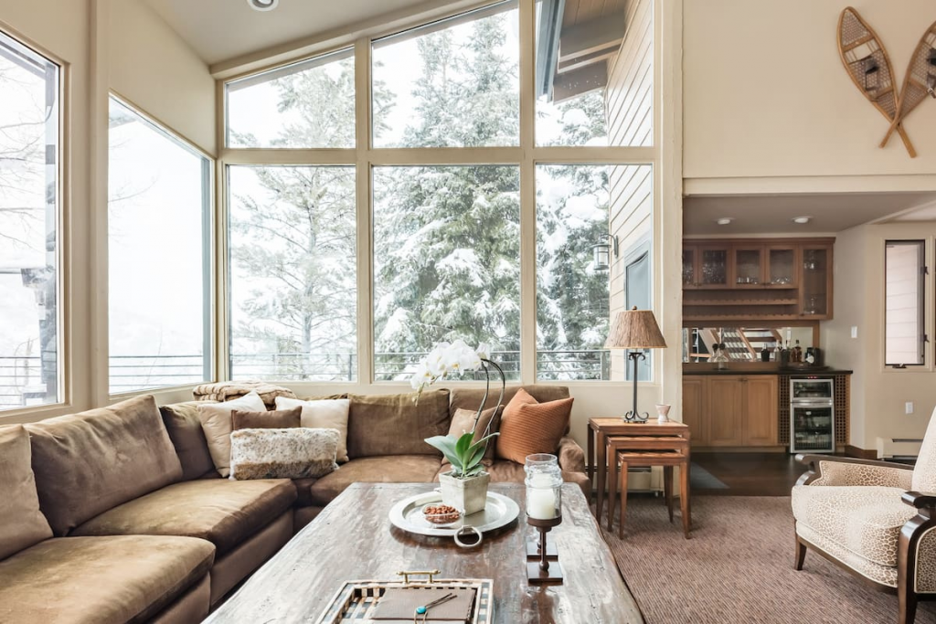 A Romantic Chalet Airbnb With Tall Windows Looking Into a Snowy Forest.