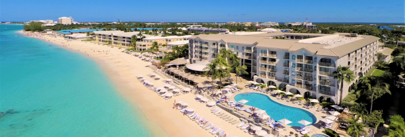 Arial shot of the bright blue ocean, beach, pool and buildings that make up Grand Cayman Marriott Beach Resort