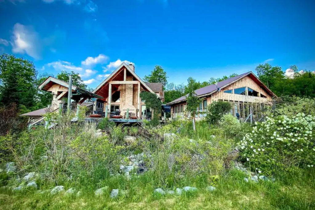 A Large Adirondacks Cabin Sits in the Background of a Green Meadow.