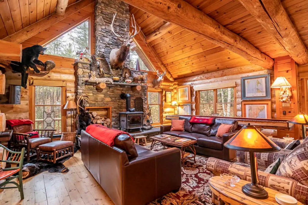 A Great Room at an Adirondacks Log Cabin Filled With Taxidermy, Warm Light, and Rustic Furnishings.