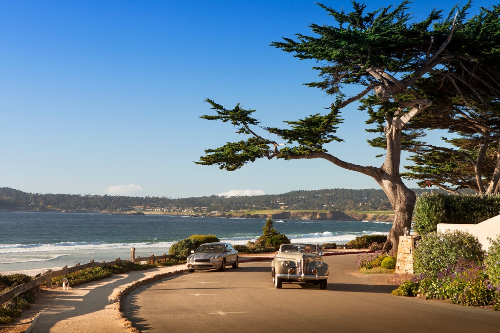 two old fashioned car driving down the road looking over the blue ocean
