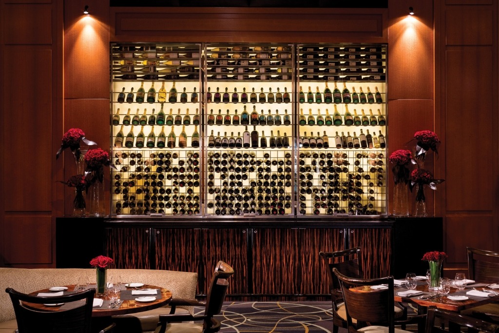 a dark brown room with a glowing bar filled with wine bottles and decorated by roses