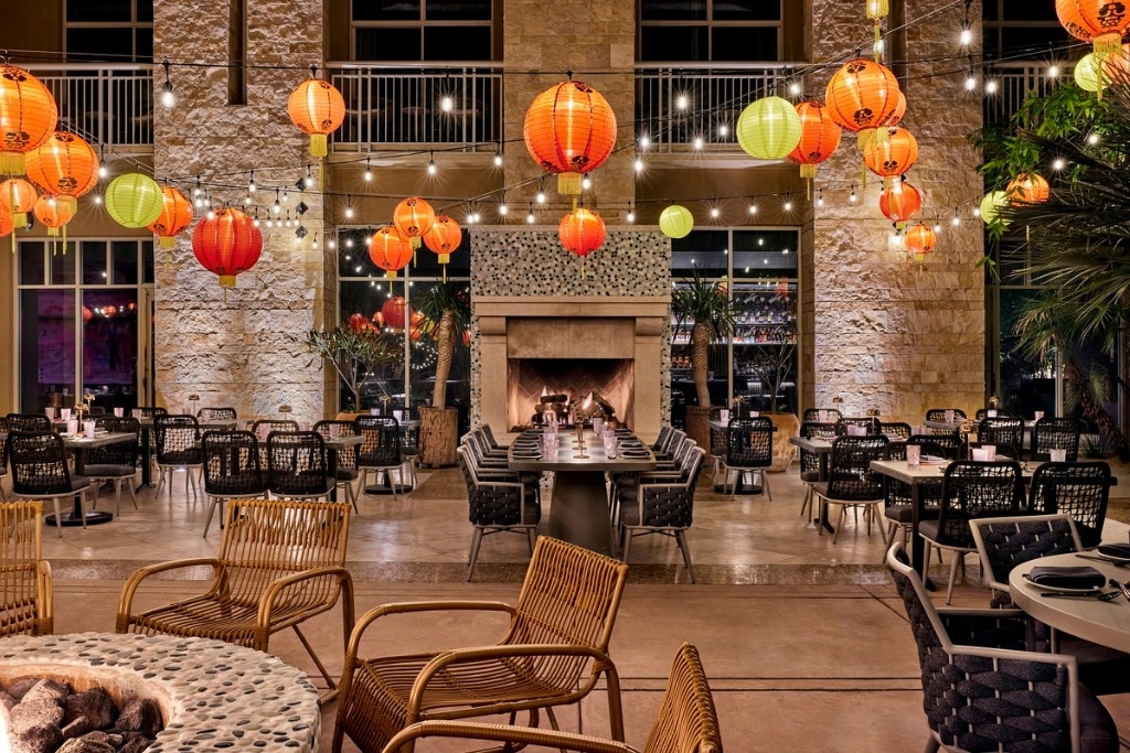 orange and green lanterns hanging from the ceiling of the restaurant while numerous tables are assembaled around