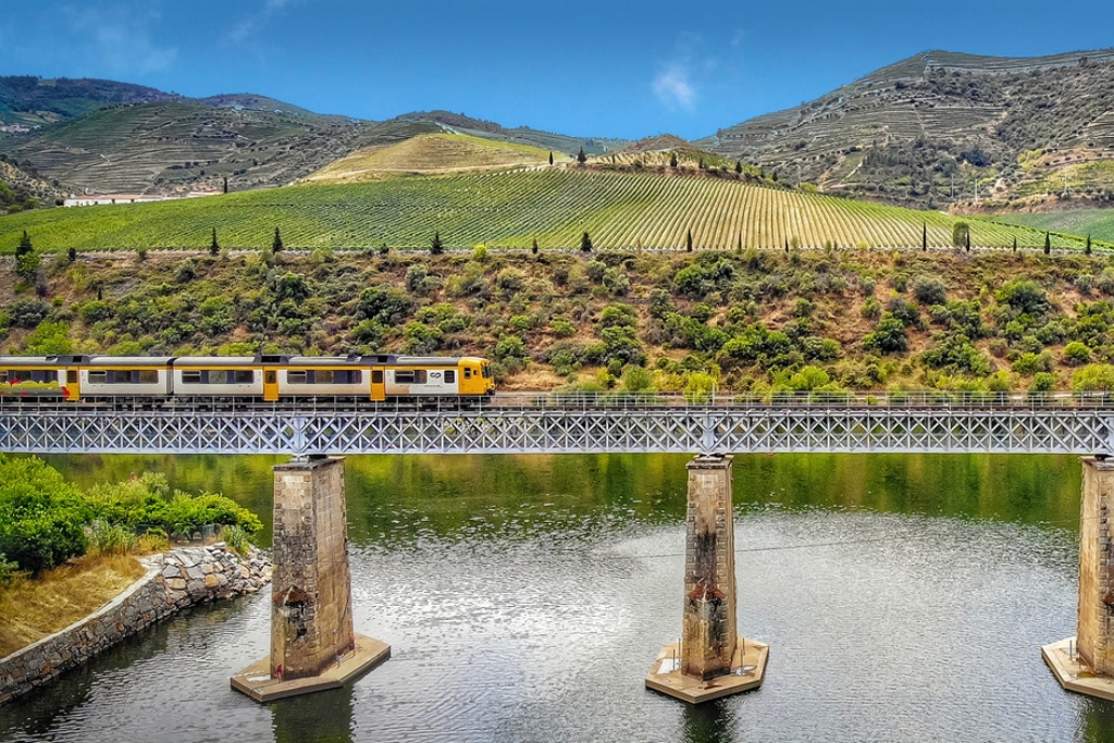 yellow train passing through vineyards and bridge in portugal over a lake