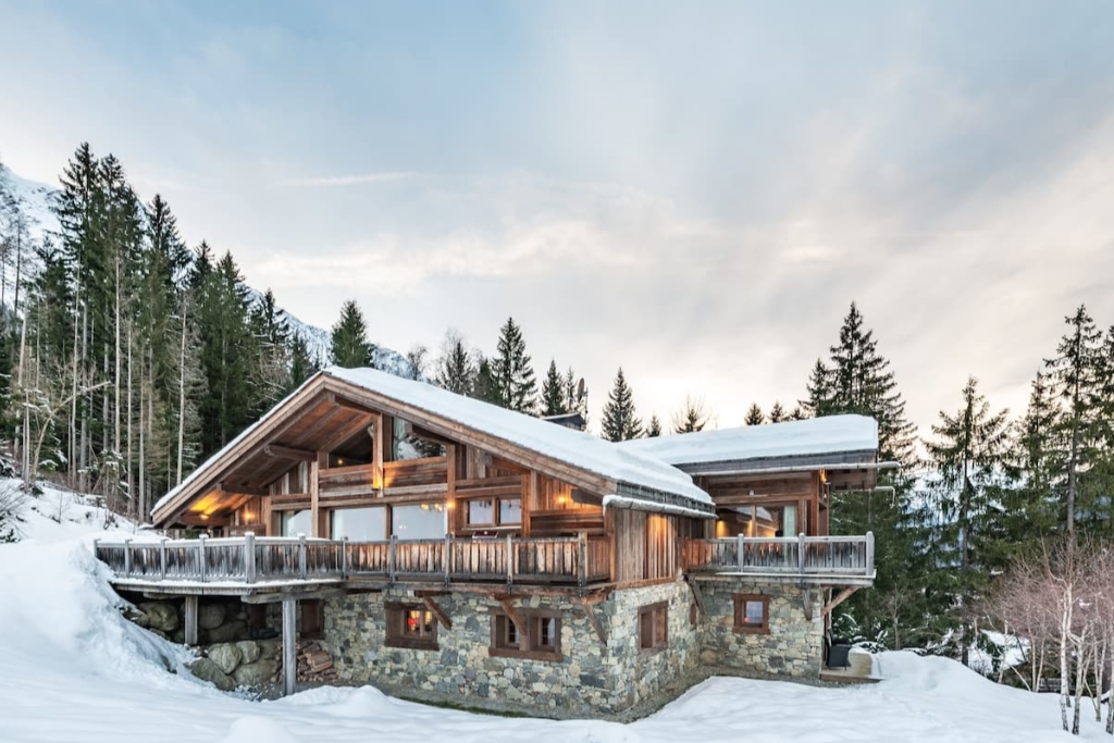 large wooden cabin in switzerland surrounded by snow with a big wrap around porch