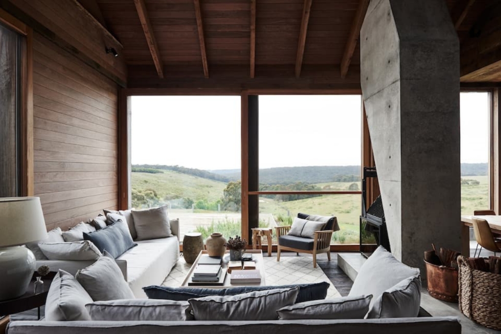 living room of a cabin in australia with grey couches open windows and a fire place
