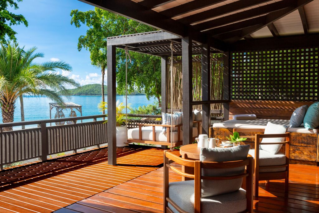 outdoor balcony of suite at hermitage bay antigua with ocean and palm tree views and plush seating