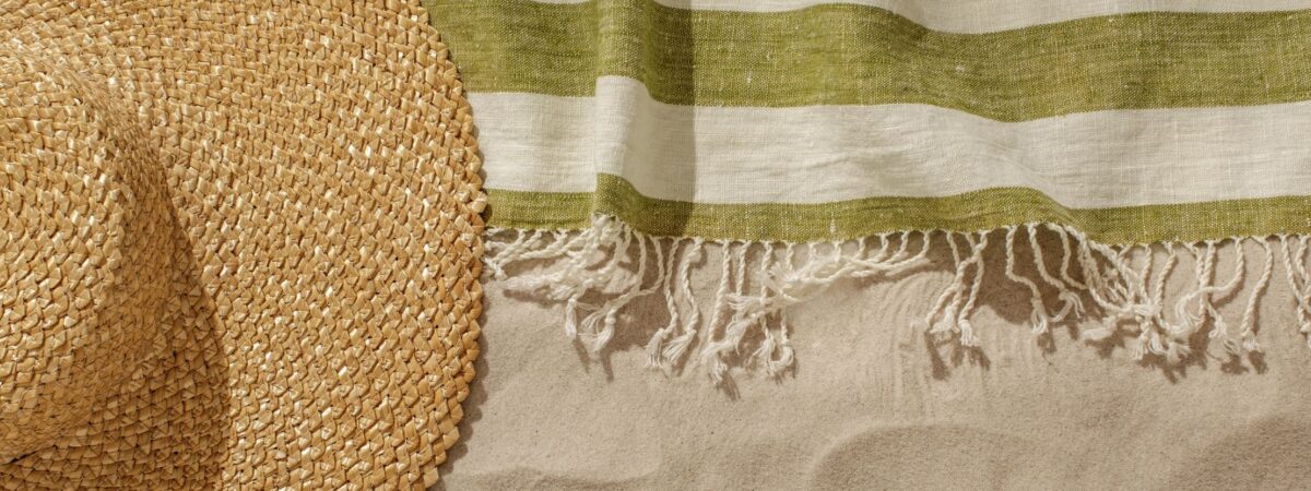 linen beach towel and straw hat in sand