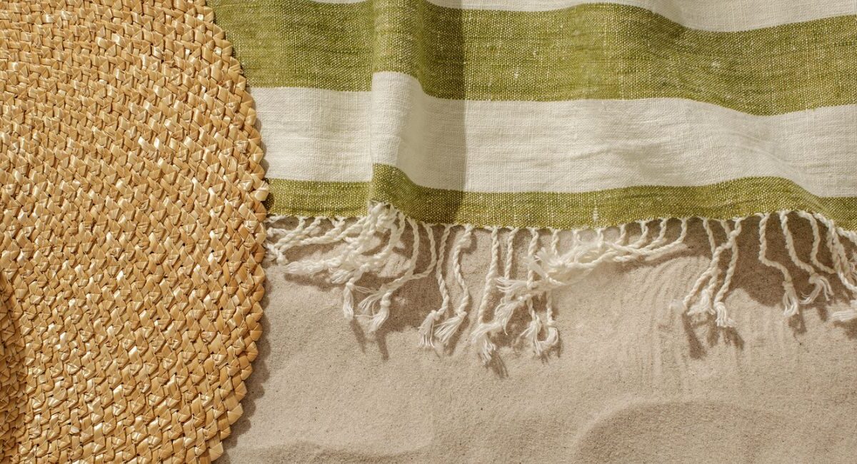 linen beach towel and straw hat in sand