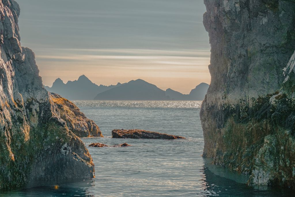 Two large rocks outlining the blue ocean with the sunrise and mountains in the horizon