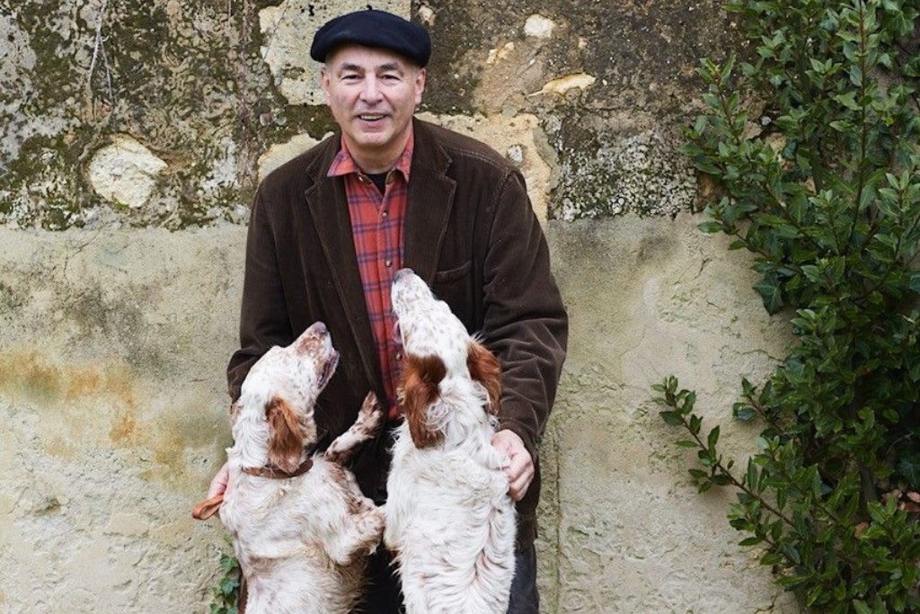 bruno eugène borie leaning against a wall outside with his two dogs jumping on him