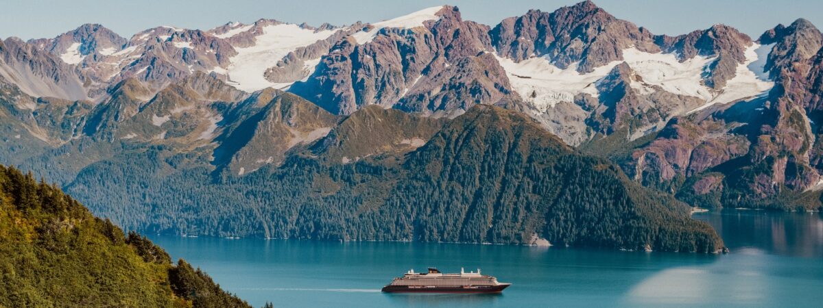 Explora journeys boat in blue water with snowy mountains and greenery behind it