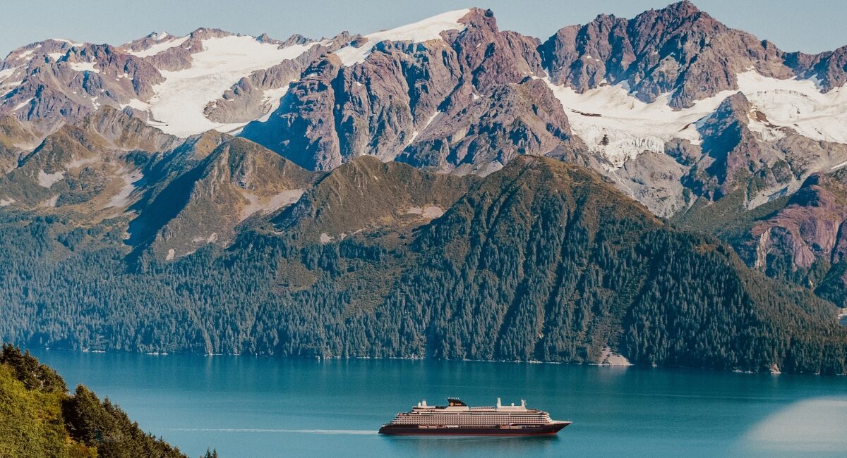 Explora journeys boat in blue water with snowy mountains and greenery behind it