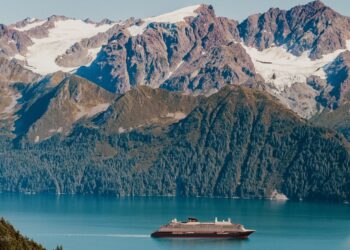 Explora journeys boat in blue water with snowy mountains and greenery behind it