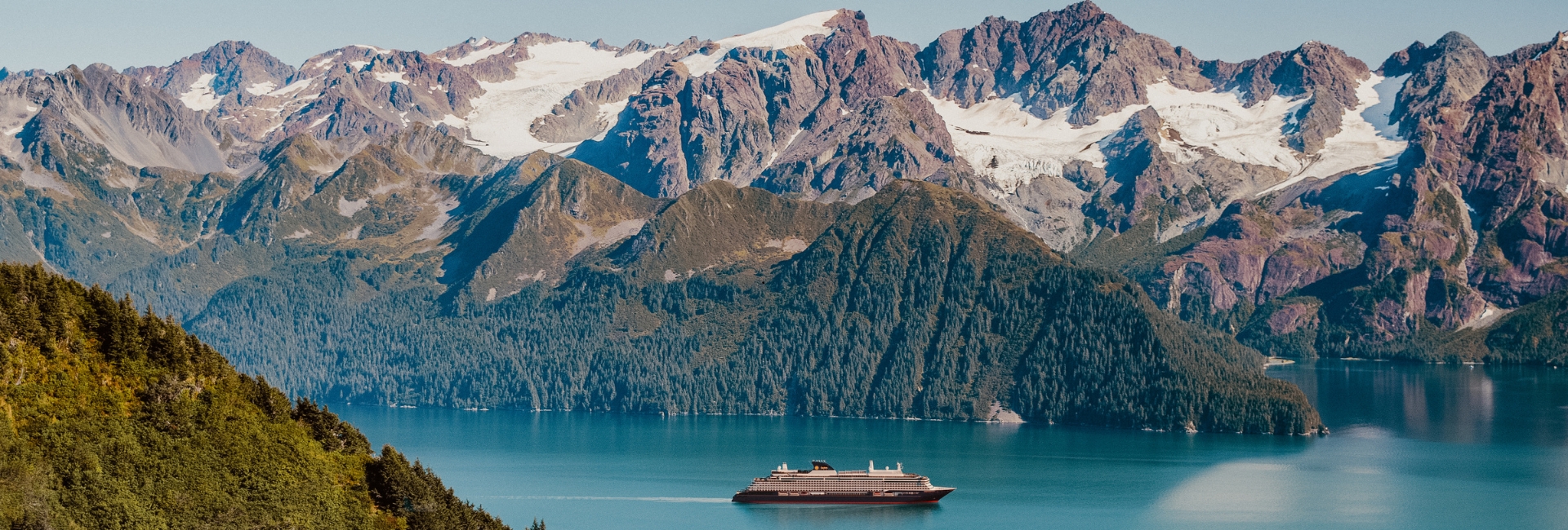 Explora journeys boat in blue water with snowy mountains and greenery behind it