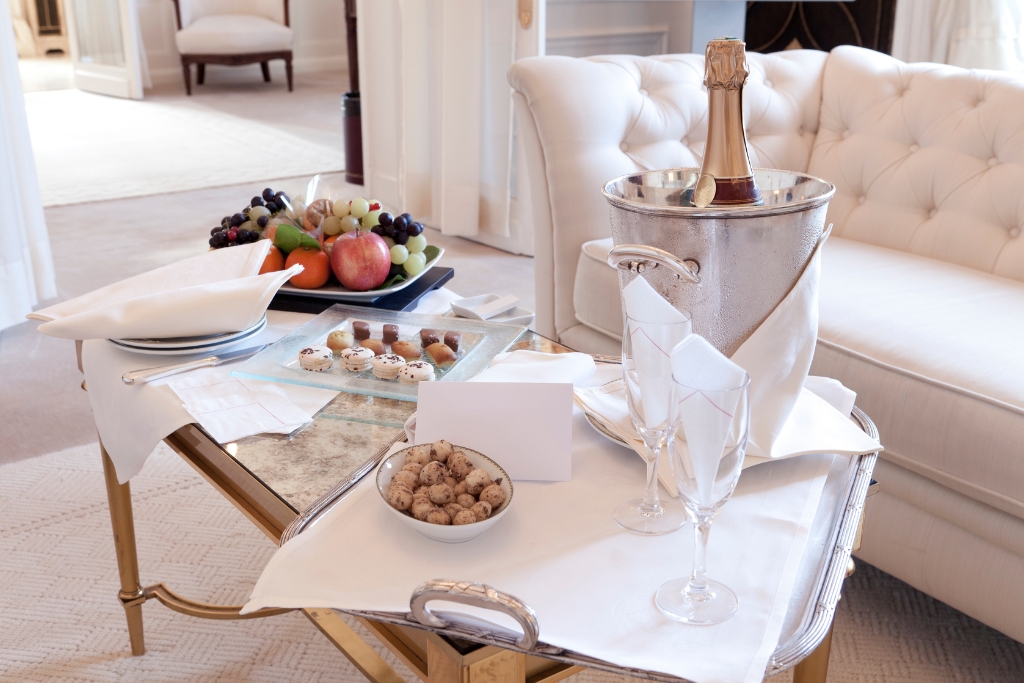 hotel room service with macaroons and fruit and a bottle of champagne surrounded by white decor 