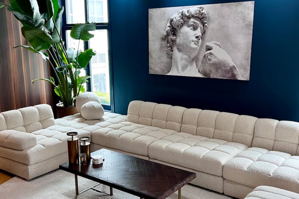 modern apartment with a white couch and large green plant and a painting of a statue hanging on the blue wall