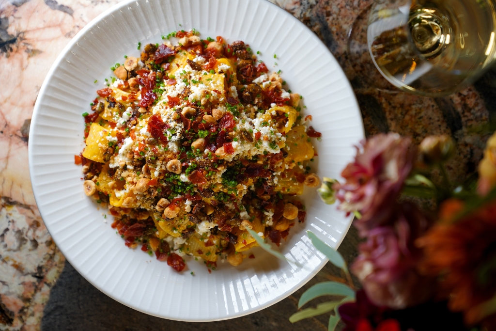 bowl of pasta seasoned with cheese and tomato and chickpea on a white plate next to a glass of white wine