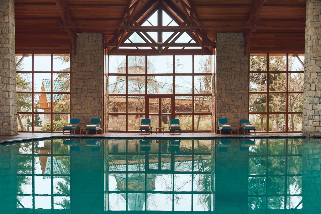indoor blue pool with floor to ceiling windows looking out onto the resort and stone panels leading up to the wooden roof