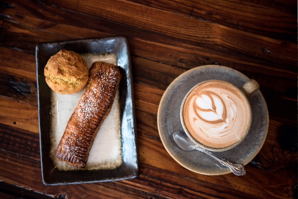 overhead view of a cup of coffee with foam art and pastries next to it