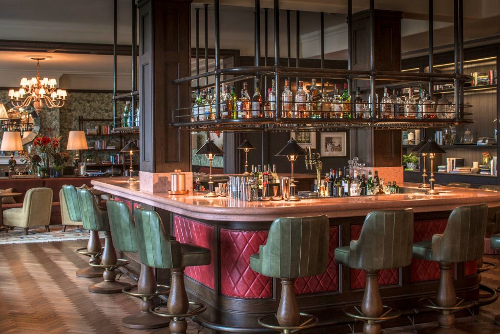 bar with green velvet chairs, red upholstered bar, black hardware, and seating room in the background
