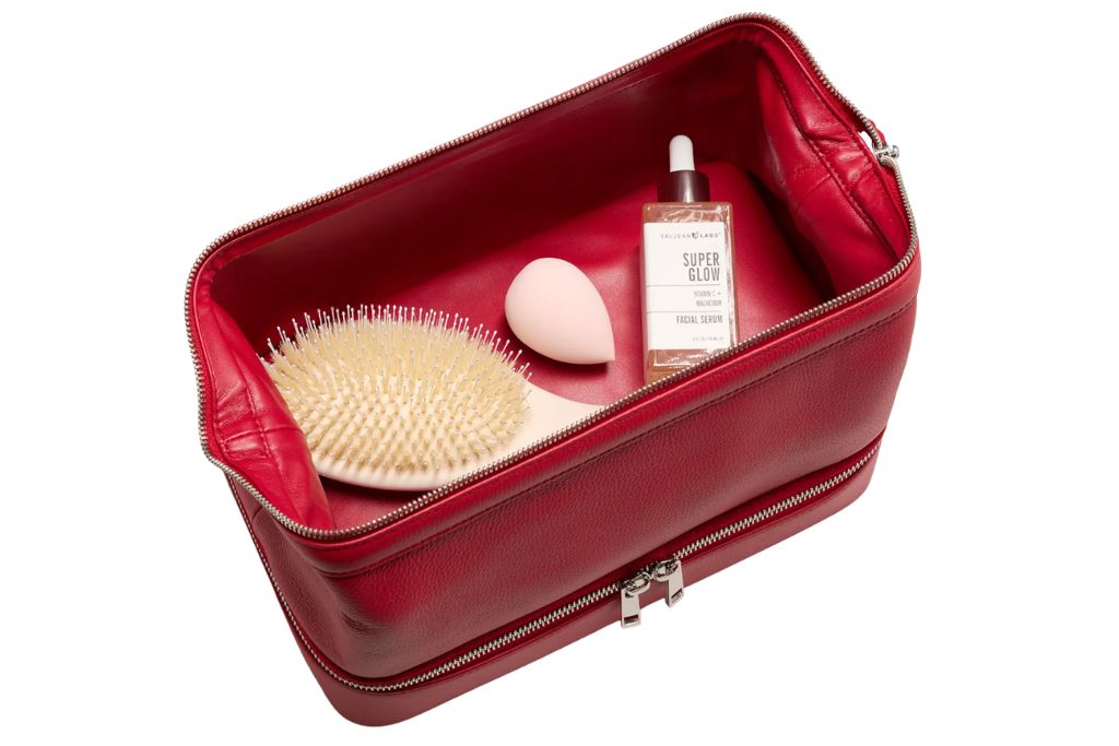 red dual compartment toiletry bag with top compartment open with products inside
