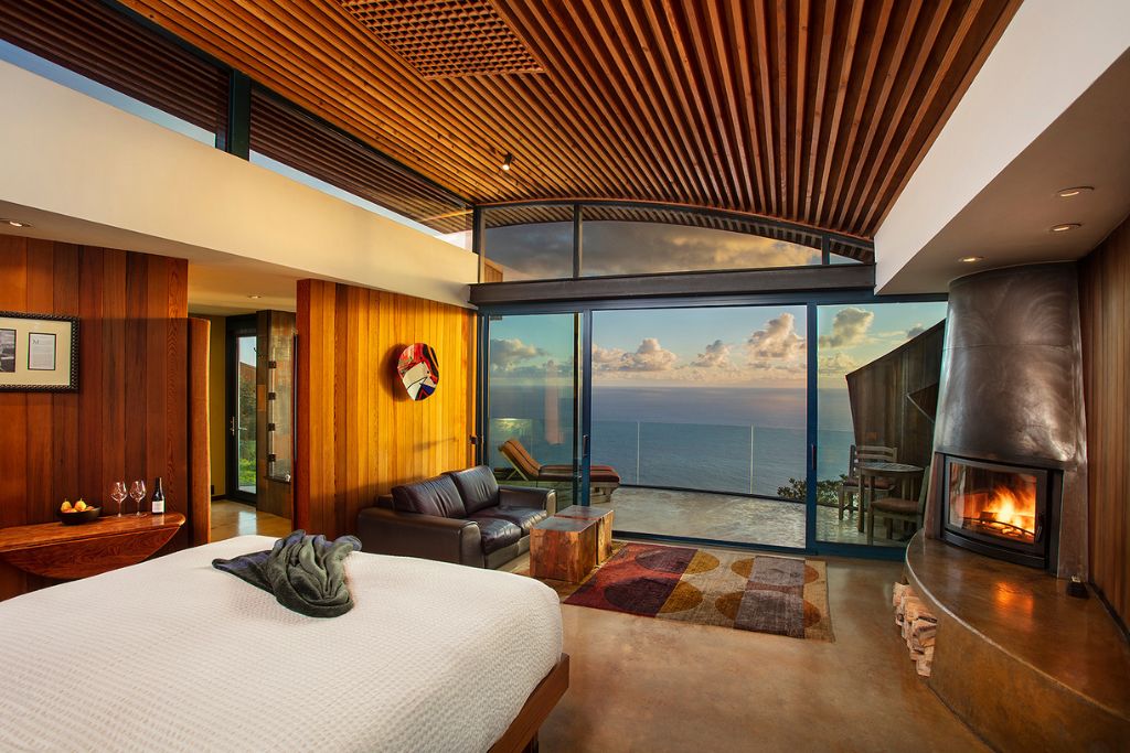 cliff house interior bed and seating area with fireplace and outdoor balcony access